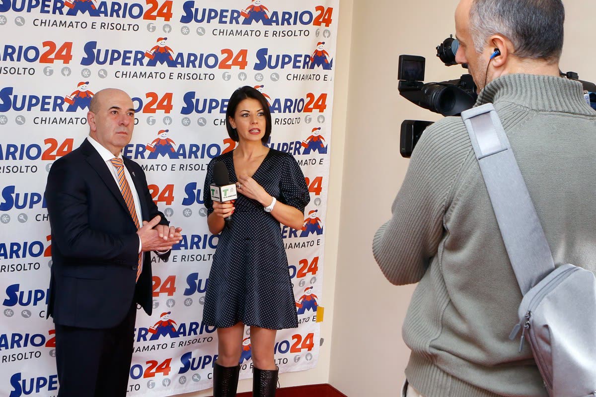 Mario intervistato in studio televisivo davanti al fondale Super Mario 24