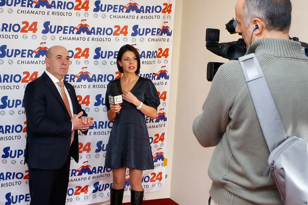 Mario intervistato in studio televisivo davanti al fondale Super Mario 24
