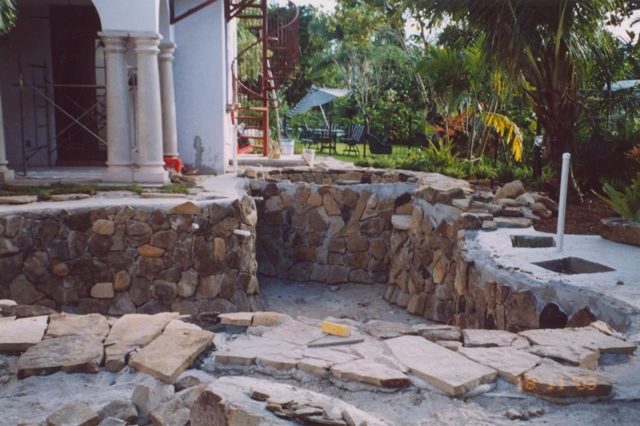 Muro in pietra terminato in un giardino, con una scala a chiocciola rossa