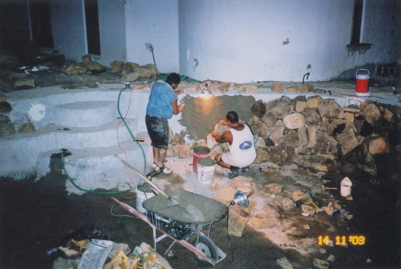 Fotografia d'archivio: uomo al lavoro su un muro in pietra, carriola in primo piano