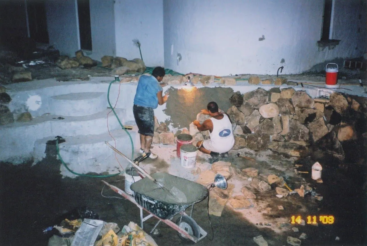 Fotografia d'archivio: uomo al lavoro su un muro in pietra, carriola in primo piano