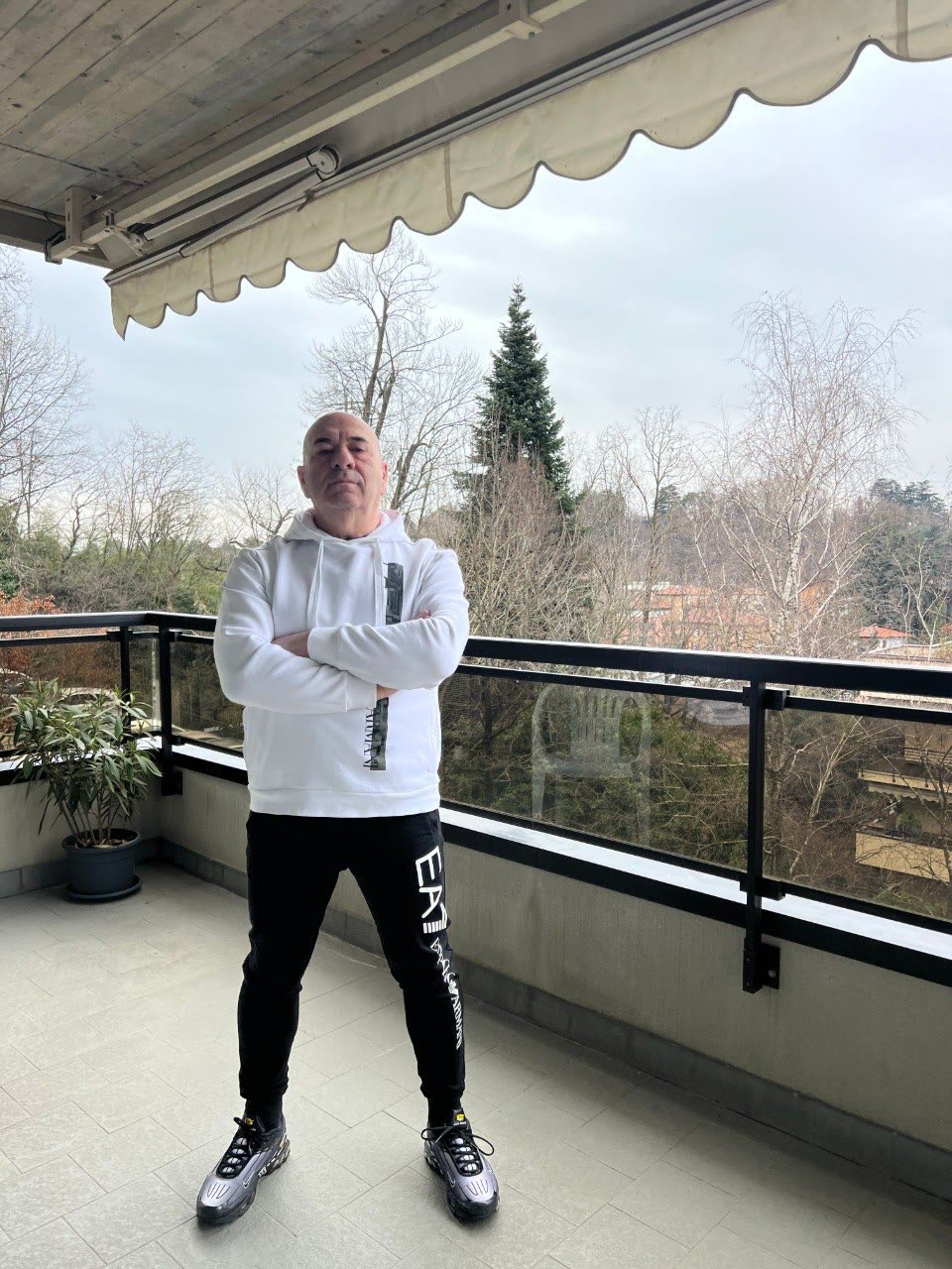 Mario in felpa bianca su un balcone, braccia conserte