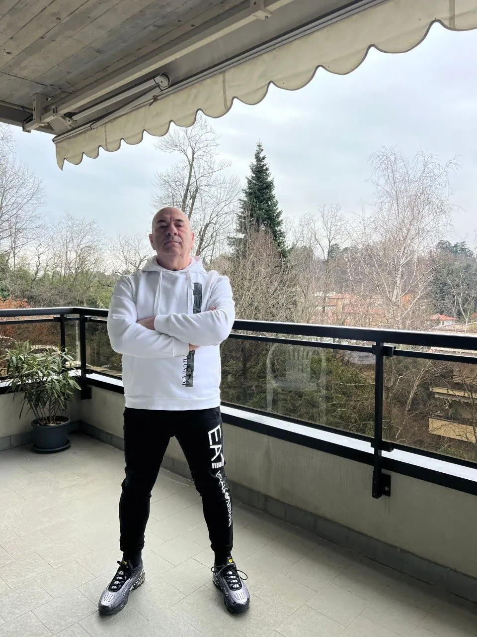 Mario in felpa bianca su un balcone, braccia conserte